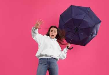 Emotional woman with umbrella caught in gust of wind on pink background