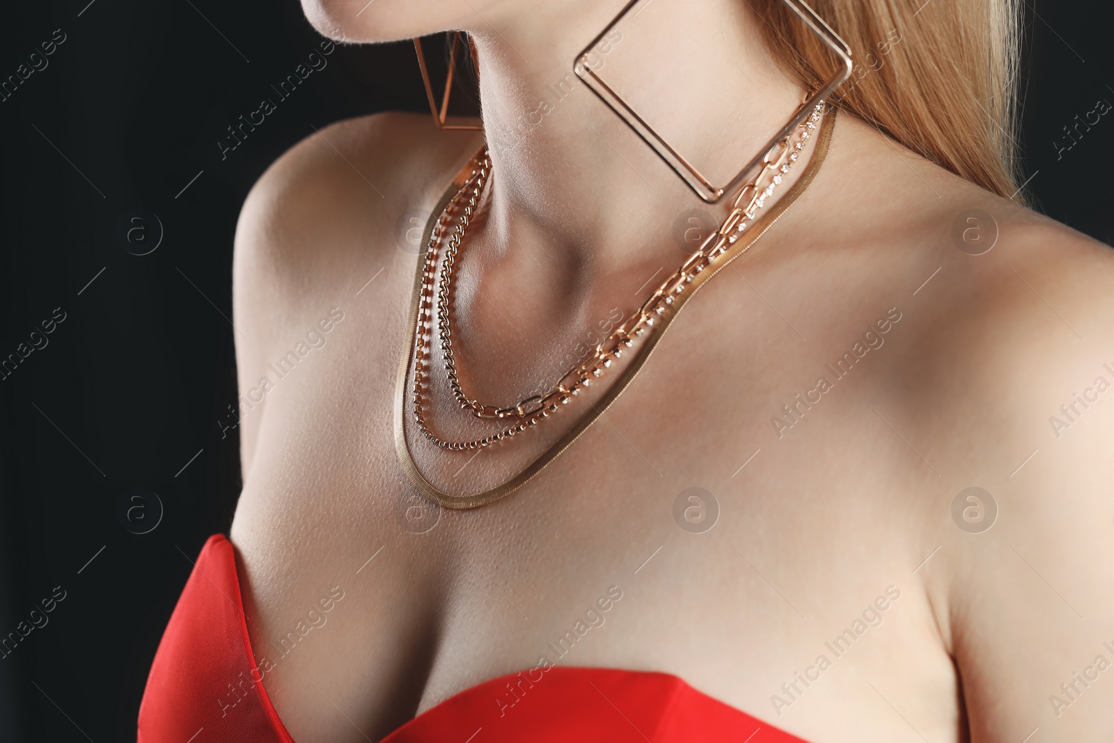 Photo of Woman wearing stylish metal chains and earrings on black background, closeup. Luxury jewelry