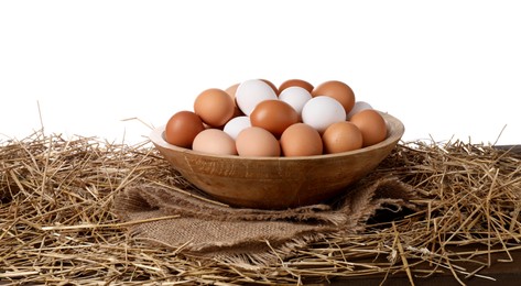 Photo of Fresh chicken eggs in bowl and dried straw on table against white background