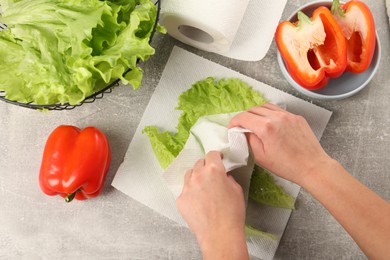 Photo of Woman wiping lettuce with paper towels at grey table, top view