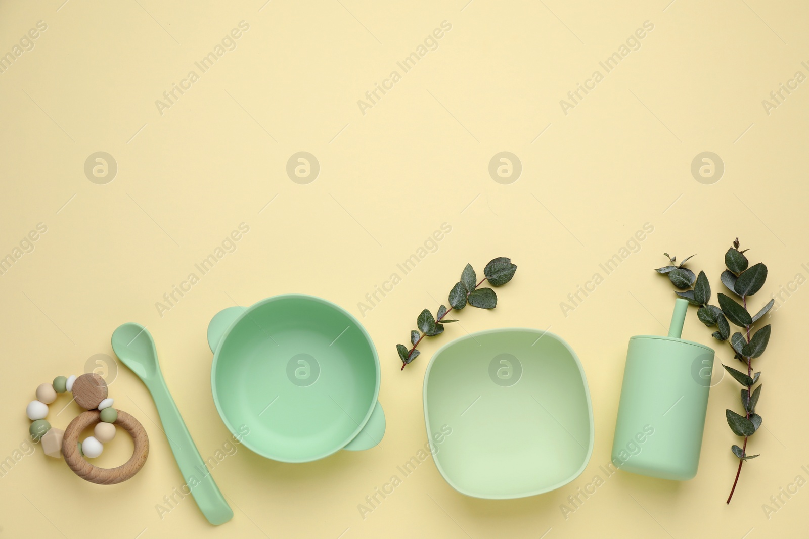 Photo of Set of plastic dishware and wooden toy on beige background, flat lay with space for text. Serving baby food