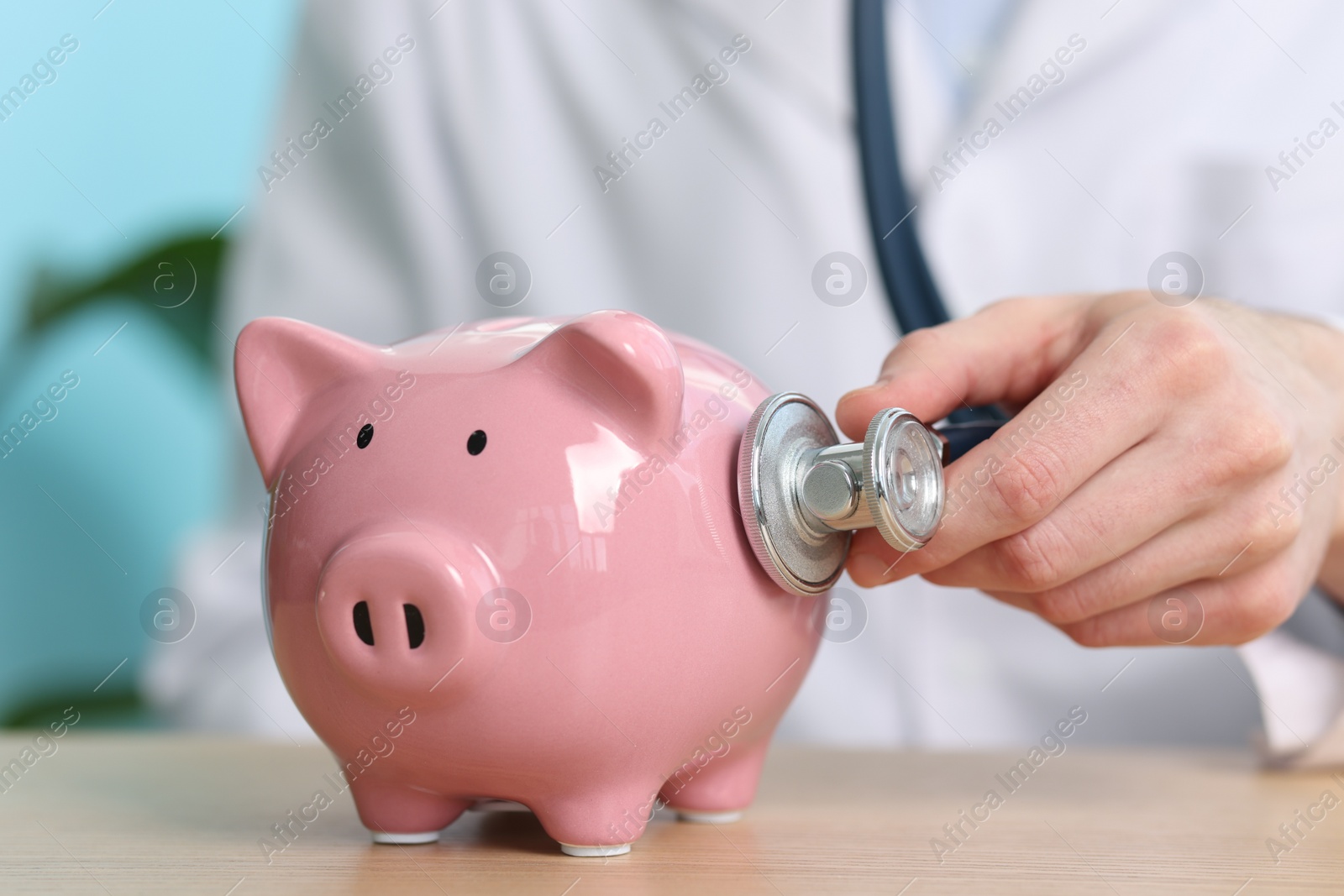 Photo of Doctor with piggy bank and stethoscope at wooden table, closeup