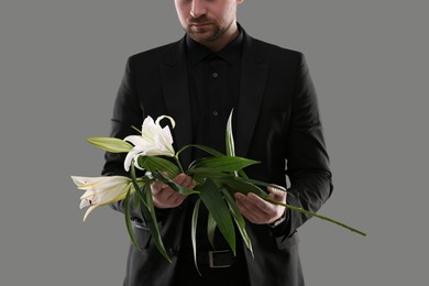 Photo of Man with white lilies on grey background, closeup. Funeral ceremony