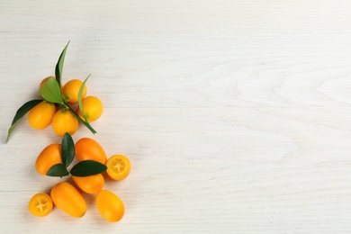 Photo of Fresh ripe kumquats with green leaves on white wooden background, flat lay. Space for text