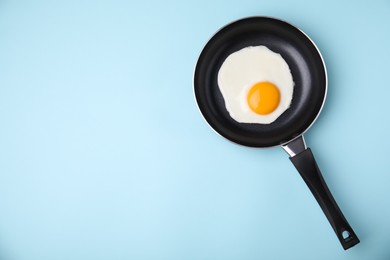 Photo of Tasty fried egg in pan on light blue background, top view. Space for text