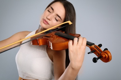 Photo of Beautiful woman playing violin on grey background, focus on hand