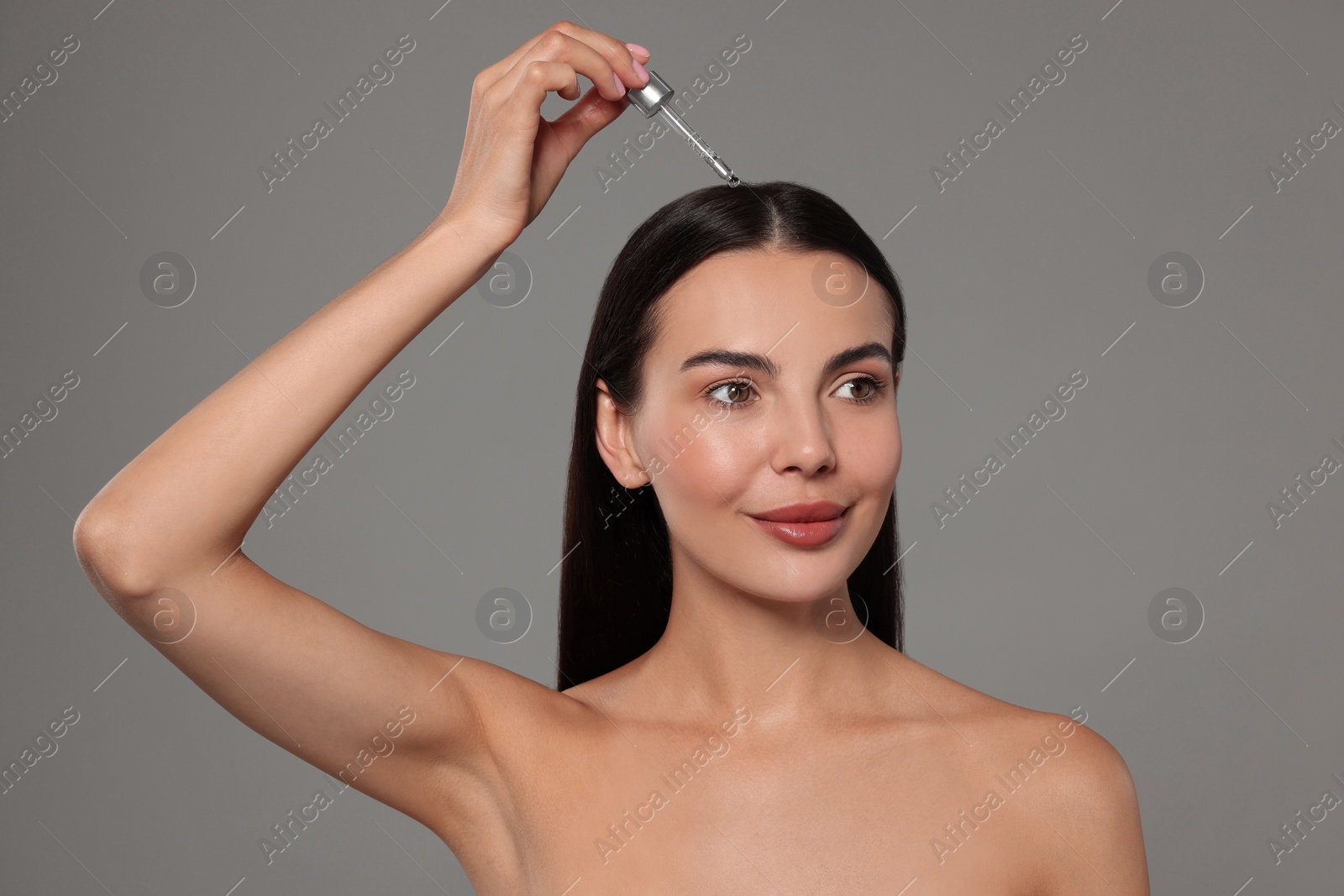 Photo of Beautiful woman applying hair serum on grey background. Cosmetic product