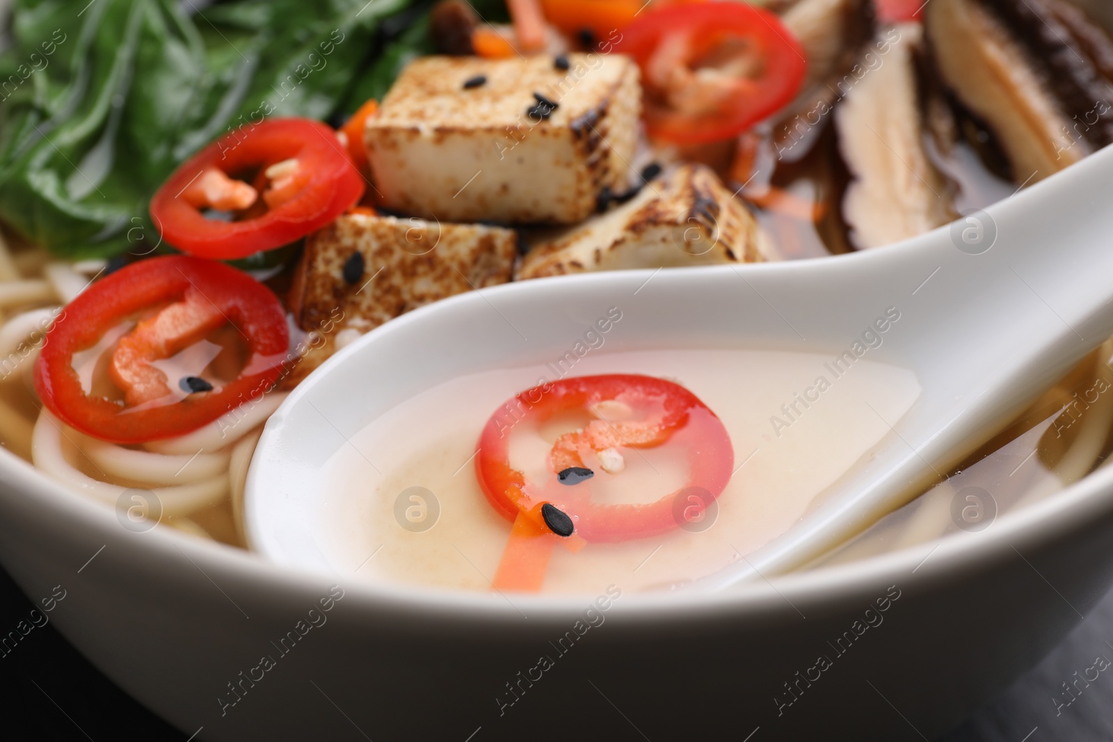 Photo of Delicious vegetarian ramen and spoon in bowl, closeup