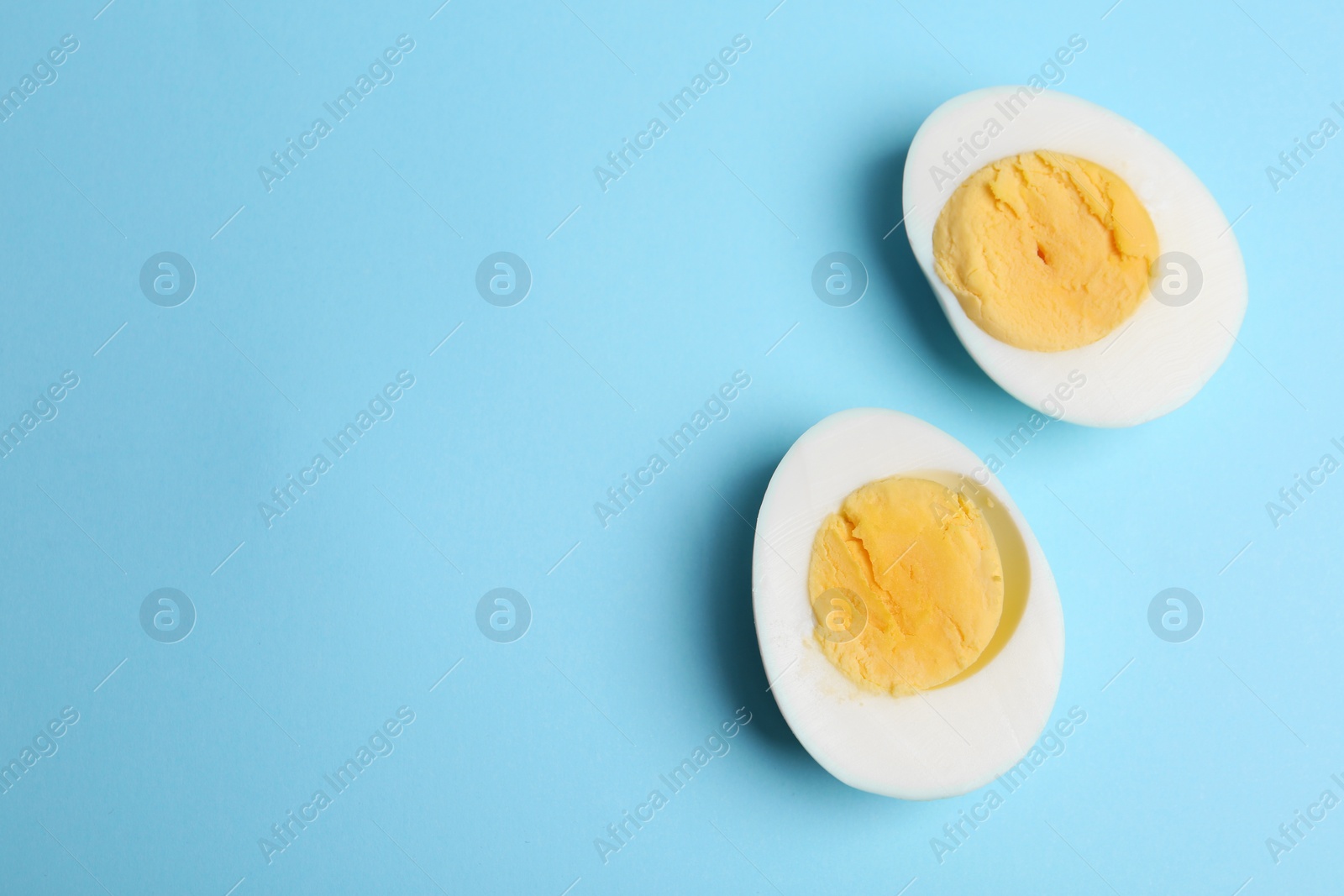 Photo of Halves of fresh hard boiled chicken egg on light blue background, flat lay. Space for text