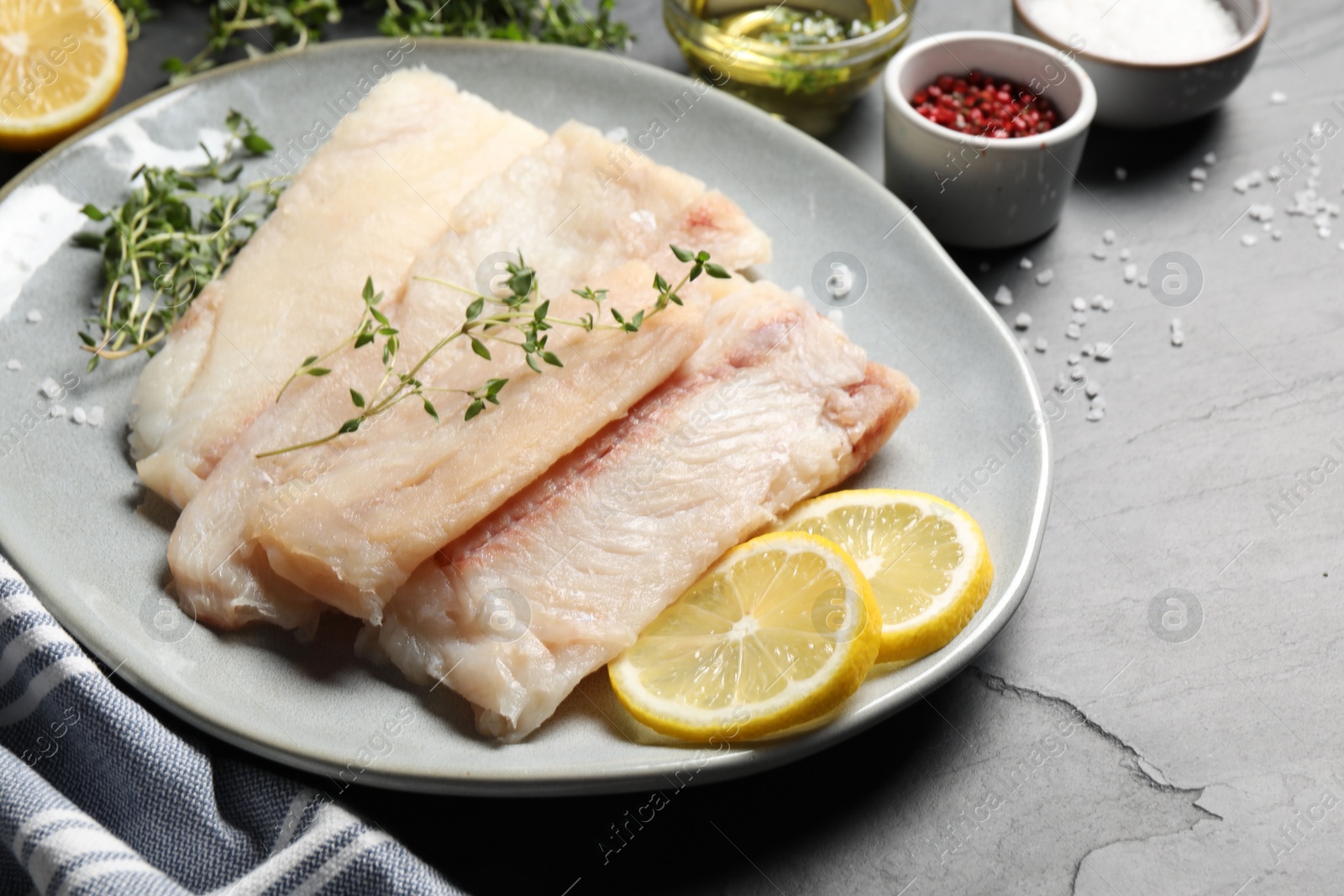 Photo of Plate with raw cod fish, microgreens, lemon and spices on grey textured table, closeup