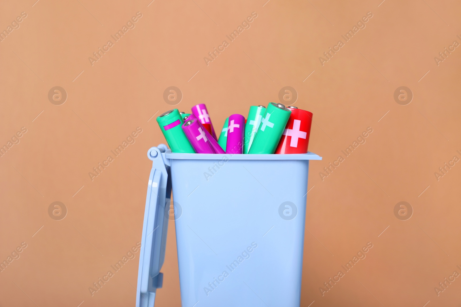 Photo of Many used batteries in recycling bin on light brown background