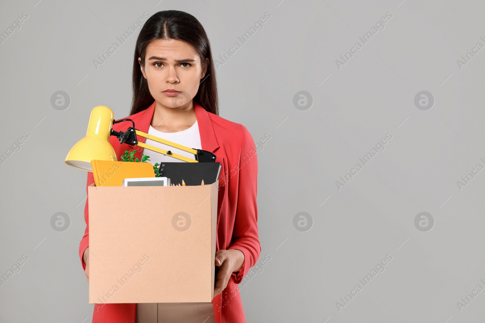 Photo of Unemployed woman with box of personal office belongings on grey background. Space for text