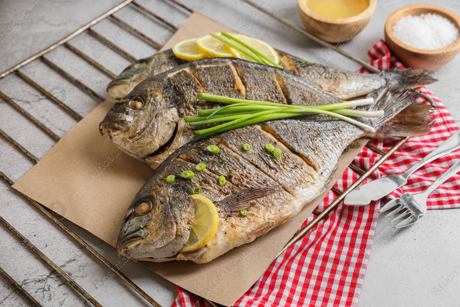 Photo of Seafood. Delicious baked fish served with green onion and lemon on light table, closeup