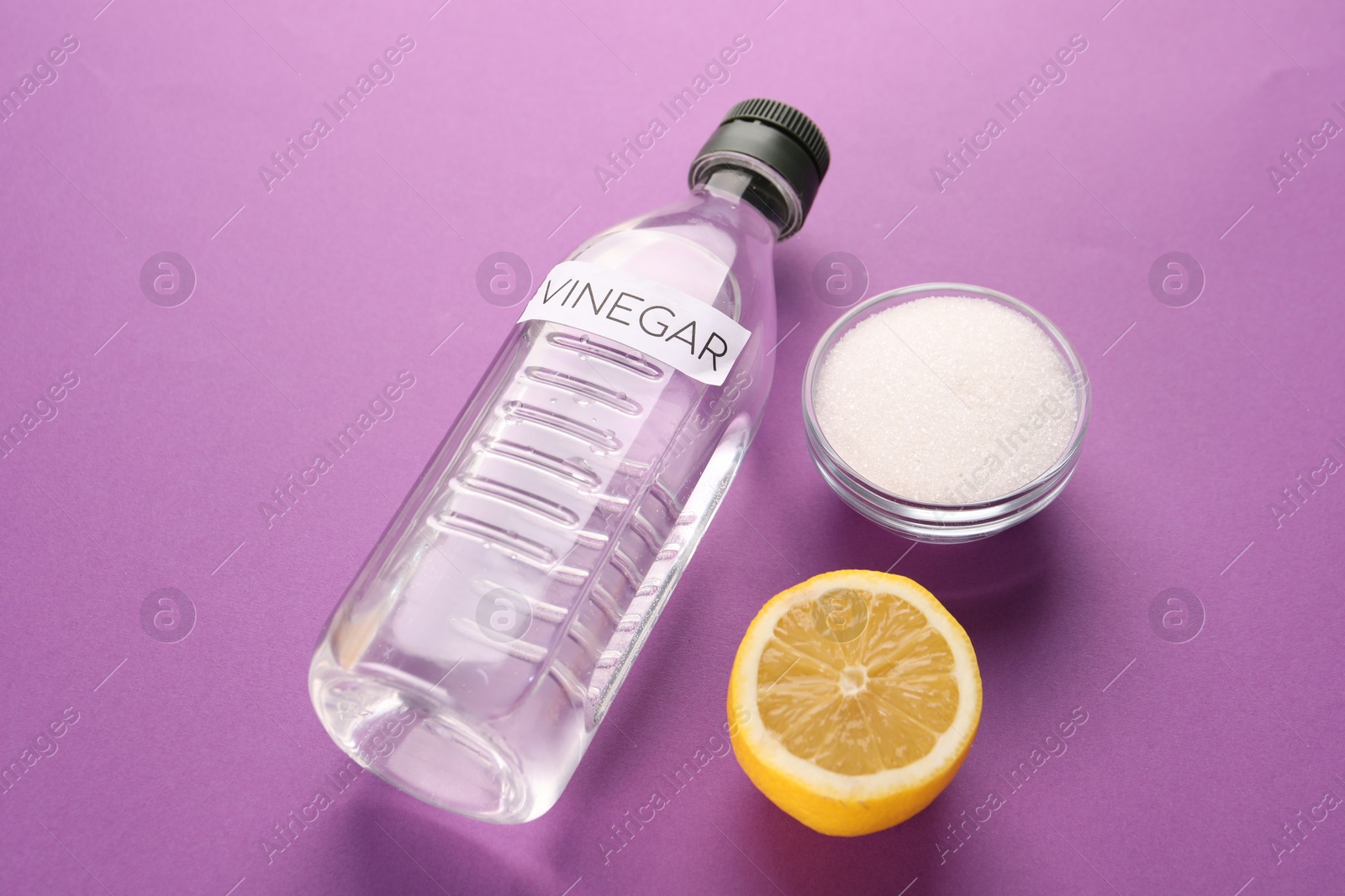 Photo of Eco friendly natural cleaners. Vinegar in bottle, cut lemon and bowl of soda on purple background