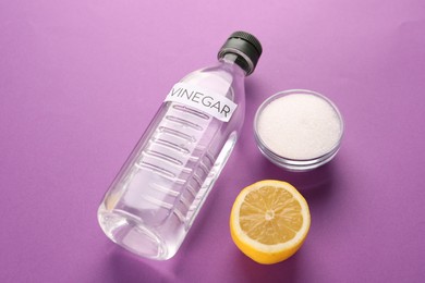 Eco friendly natural cleaners. Vinegar in bottle, cut lemon and bowl of soda on purple background