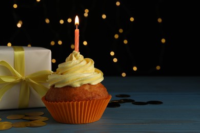 Delicious birthday cupcake with candle near gift box on wooden table against blurred festive lights, space for text