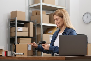 Photo of Seller with scanner reading parcel barcode at workplace. Online store