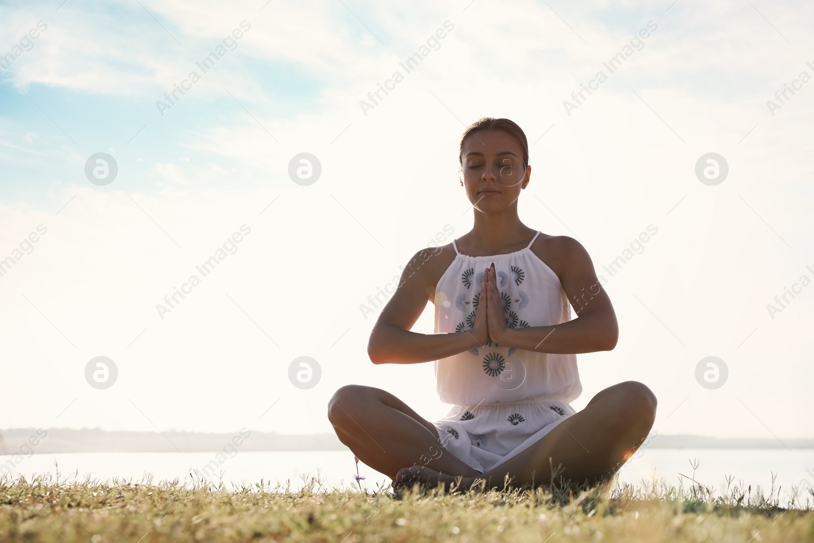 Photo of Young woman meditating near river at sunset, space for text. Nature healing power