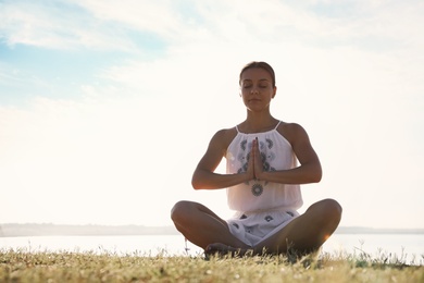 Photo of Young woman meditating near river at sunset, space for text. Nature healing power