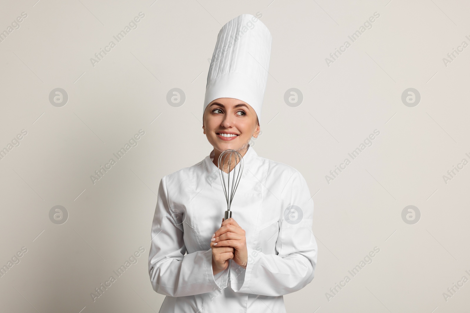 Photo of Happy professional confectioner in uniform holding whisk on light grey background