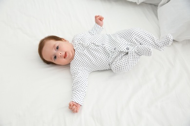 Photo of Adorable baby in cute footie on white sheet, above view