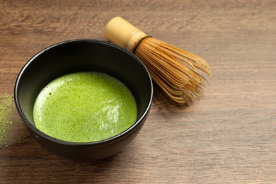 Photo of Cup of fresh matcha tea, green powder and bamboo whisk on wooden table, space for text