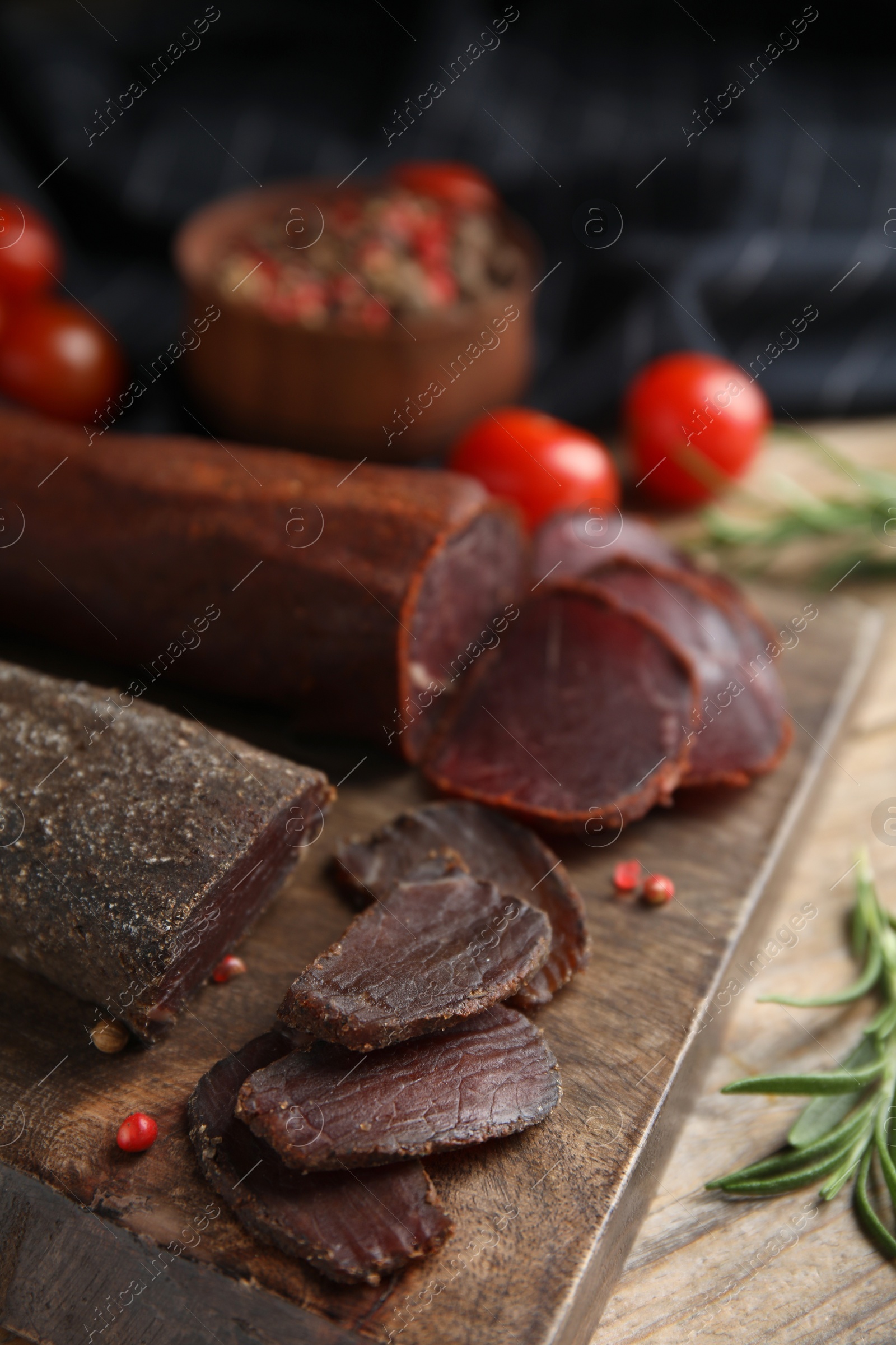 Photo of Delicious dry-cured beef basturma with rosemary and peppercorns on wooden table, closeup