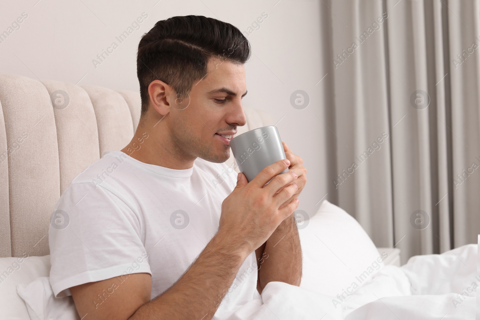 Photo of Happy man with cup of hot drink in bed at home