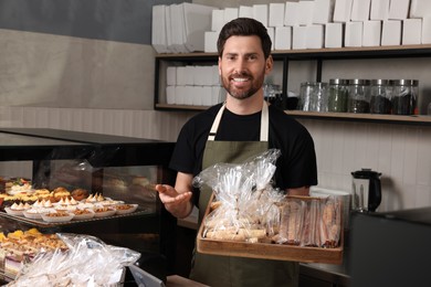 Photo of Happy seller with pastries at cashier desk in bakery shop