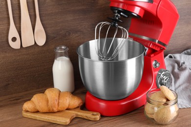 Photo of Modern red stand mixer, croissant and cookies on wooden table