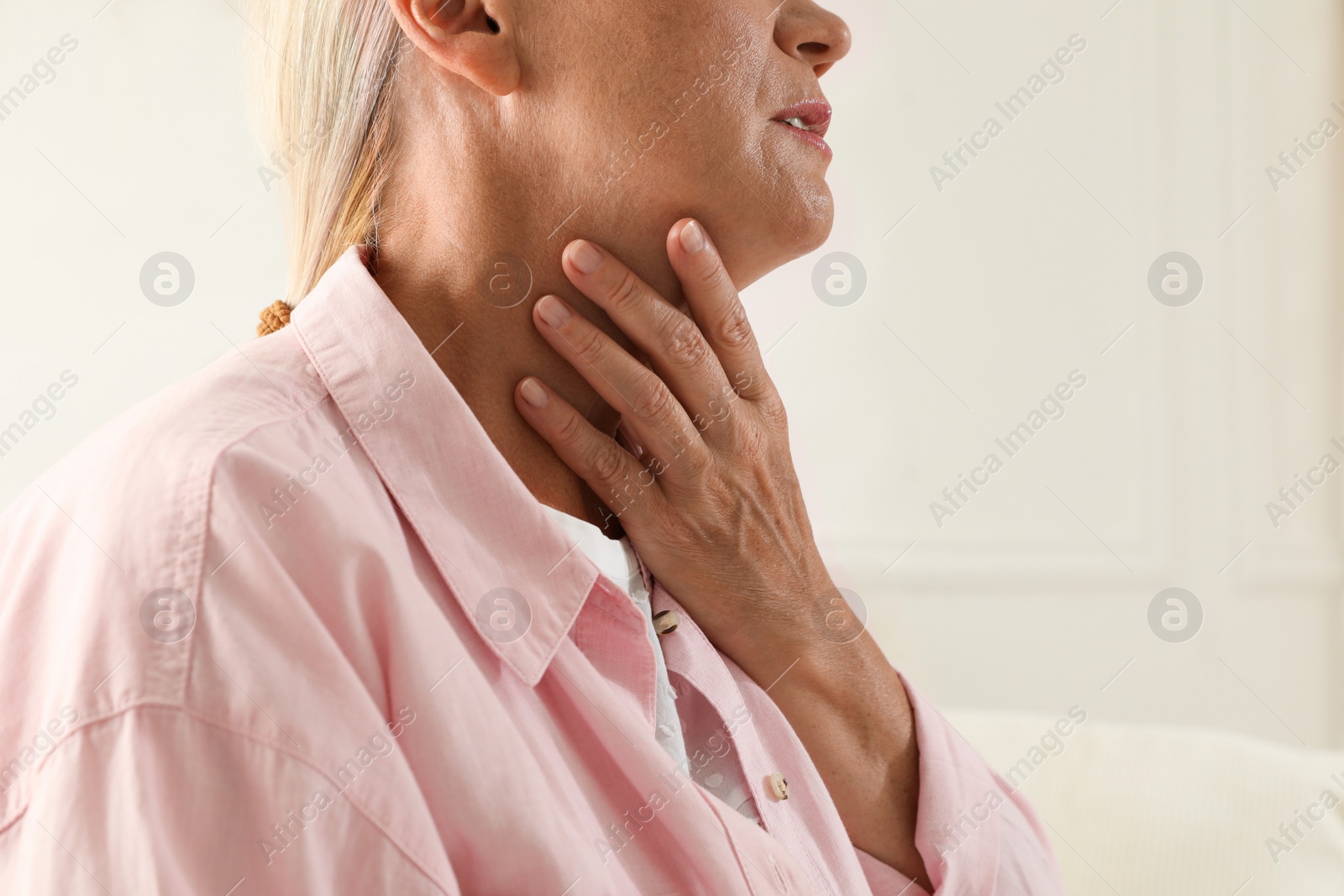 Photo of Mature woman doing thyroid self examination on light background, closeup