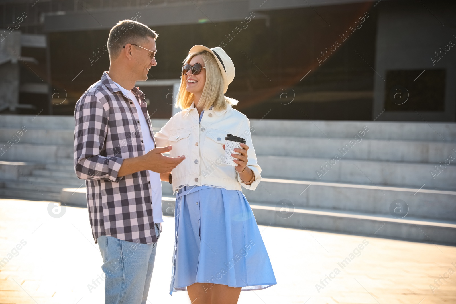 Photo of Happy couple with drink walking along city street on summer day