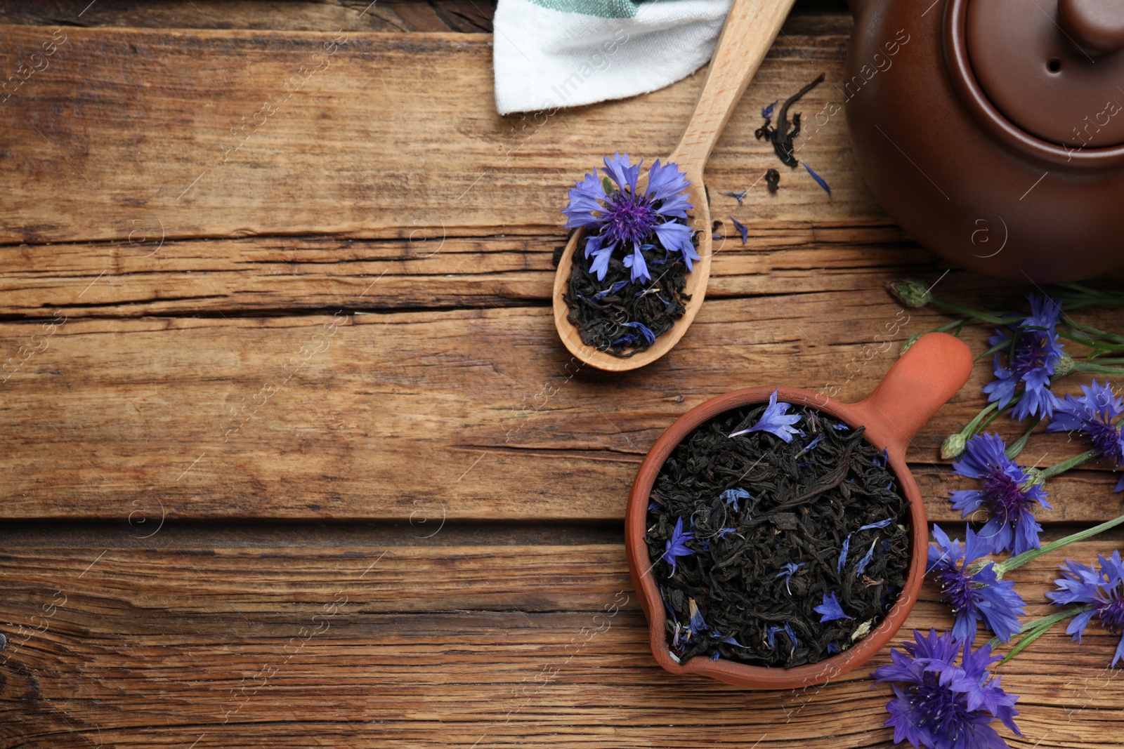 Photo of Flat lay composition with dry tea leaves and cornflowers on wooden table. Space for text