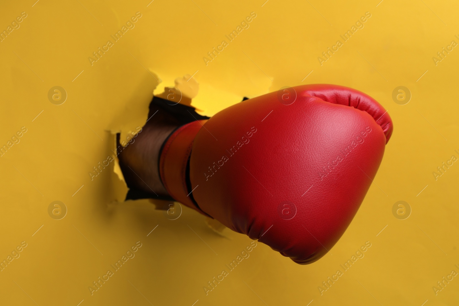 Photo of Man breaking through yellow paper with boxing glove, closeup