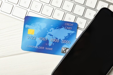 Credit card, computer keyboard and smartphone on white wooden table, closeup