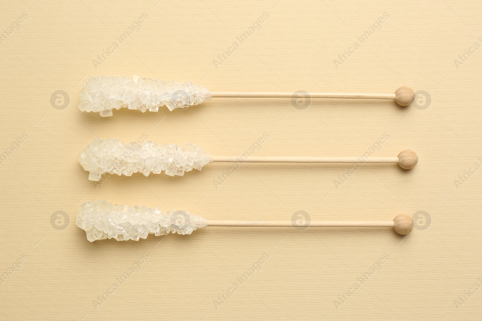 Photo of Wooden sticks with sugar crystals on beige background, flat lay. Tasty rock candies