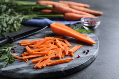 Photo of Cut raw carrot and marble board on grey table, closeup