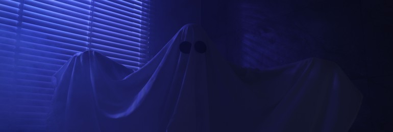 Photo of Creepy ghost. Woman covered with sheet near window in blue light