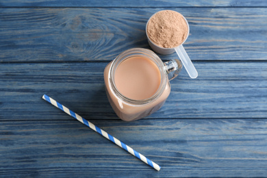 Photo of Protein shake, powder and straw on blue wooden table, flat lay