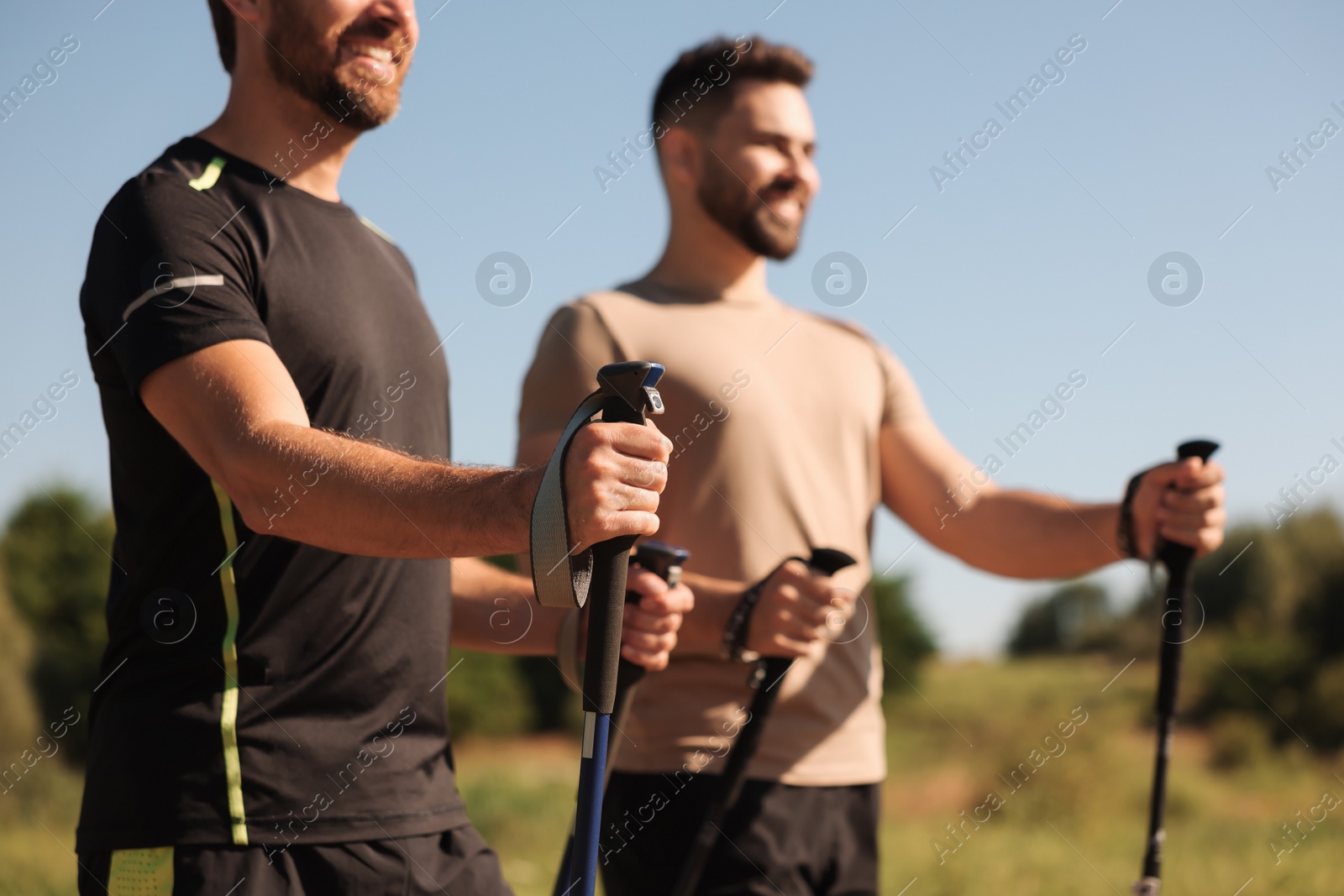 Photo of Men practicing Nordic walking with poles outdoors on sunny day, selective focus