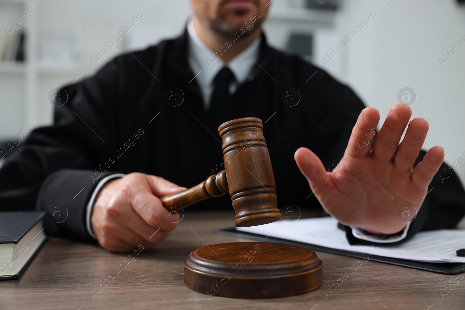 Photo of Judge with gavel and papers sitting at wooden table indoors, closeup