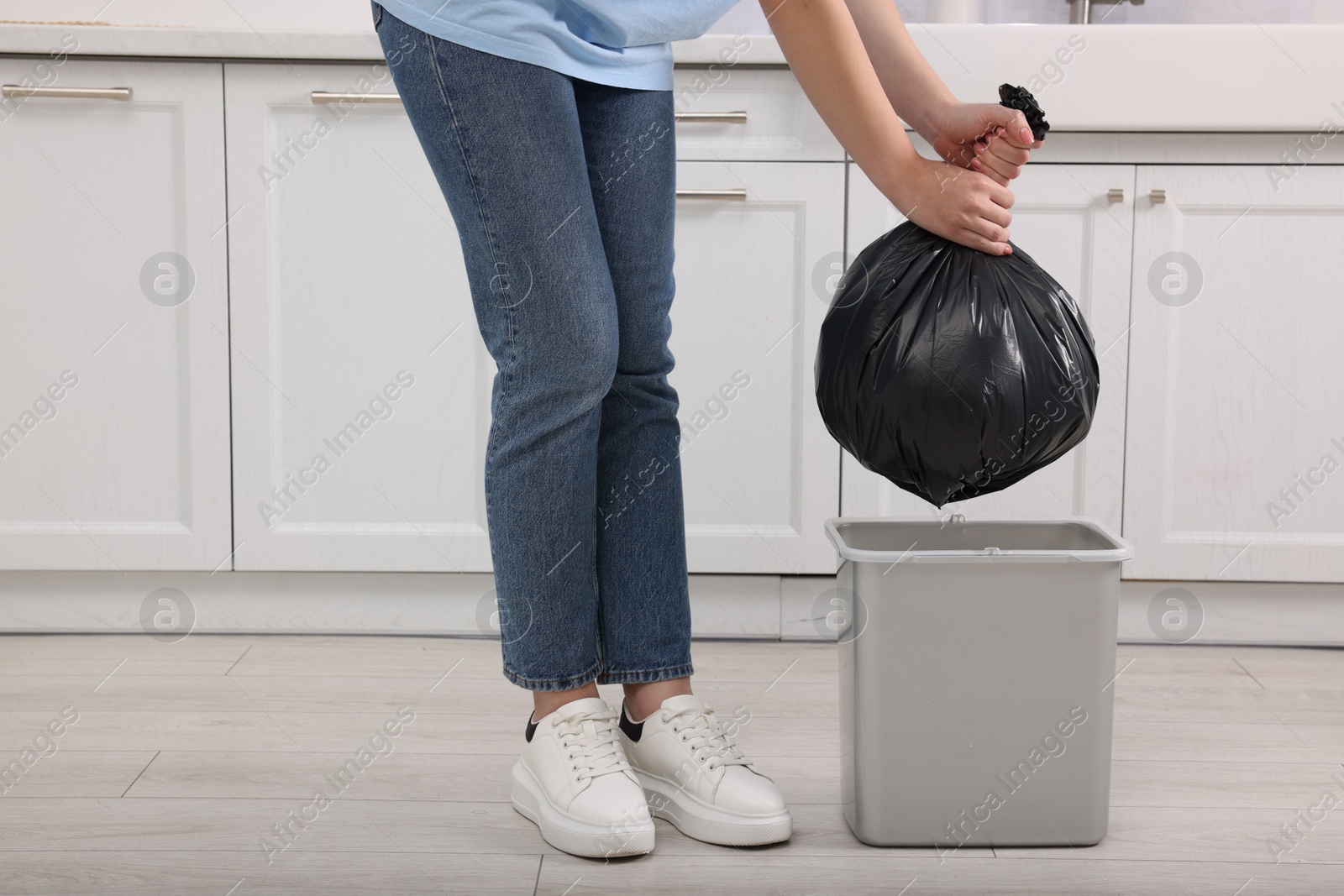 Photo of Woman taking garbage bag out of trash bin in kitchen, closeup