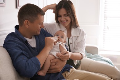 Photo of Happy couple holding their cute little baby with pacifier at home