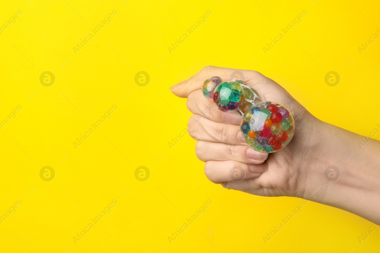 Photo of Woman squeezing colorful slime on yellow background, closeup. Antistress toy