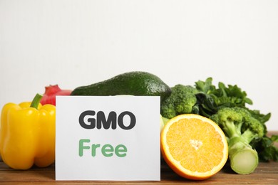 Photo of Tasty fresh GMO free products and paper card on wooden table against light background