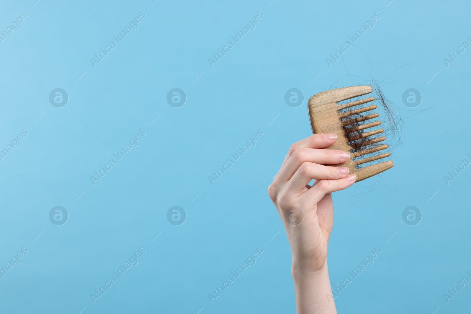 Photo of Woman holding comb with lost hair on light blue background, closeup and space for text. Alopecia problem