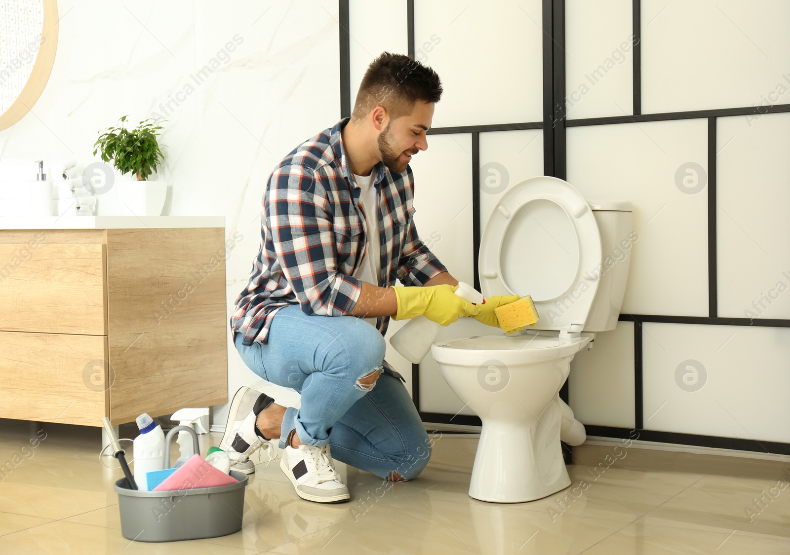 Photo of Young man cleaning toilet bowl in bathroom