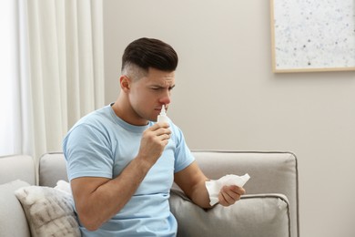 Photo of Ill man with paper tissue using nasal spray on sofa at home
