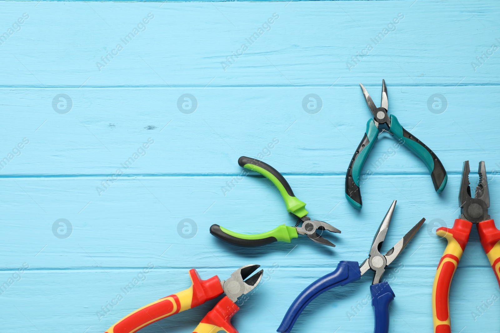 Photo of Different pliers on light blue wooden table, flat lay. Space for text