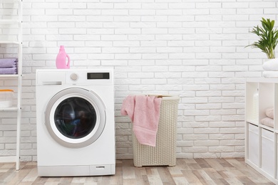 Photo of Modern washing machine near brick wall in laundry room interior, space for text